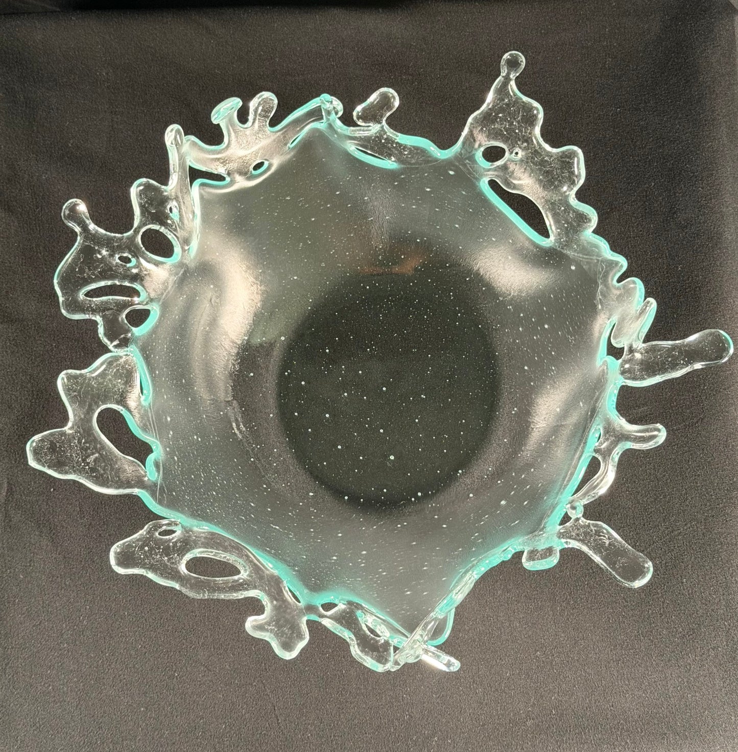 Decorative glass bowl with cut-out designs resembling splashing water on a black background