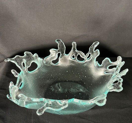 Decorative glass bowl with cut-out designs resembling splashing water on a dark background