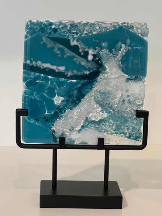 Glass panel in stand with deep blues, white and clear showing a wave crashing in the ocean.