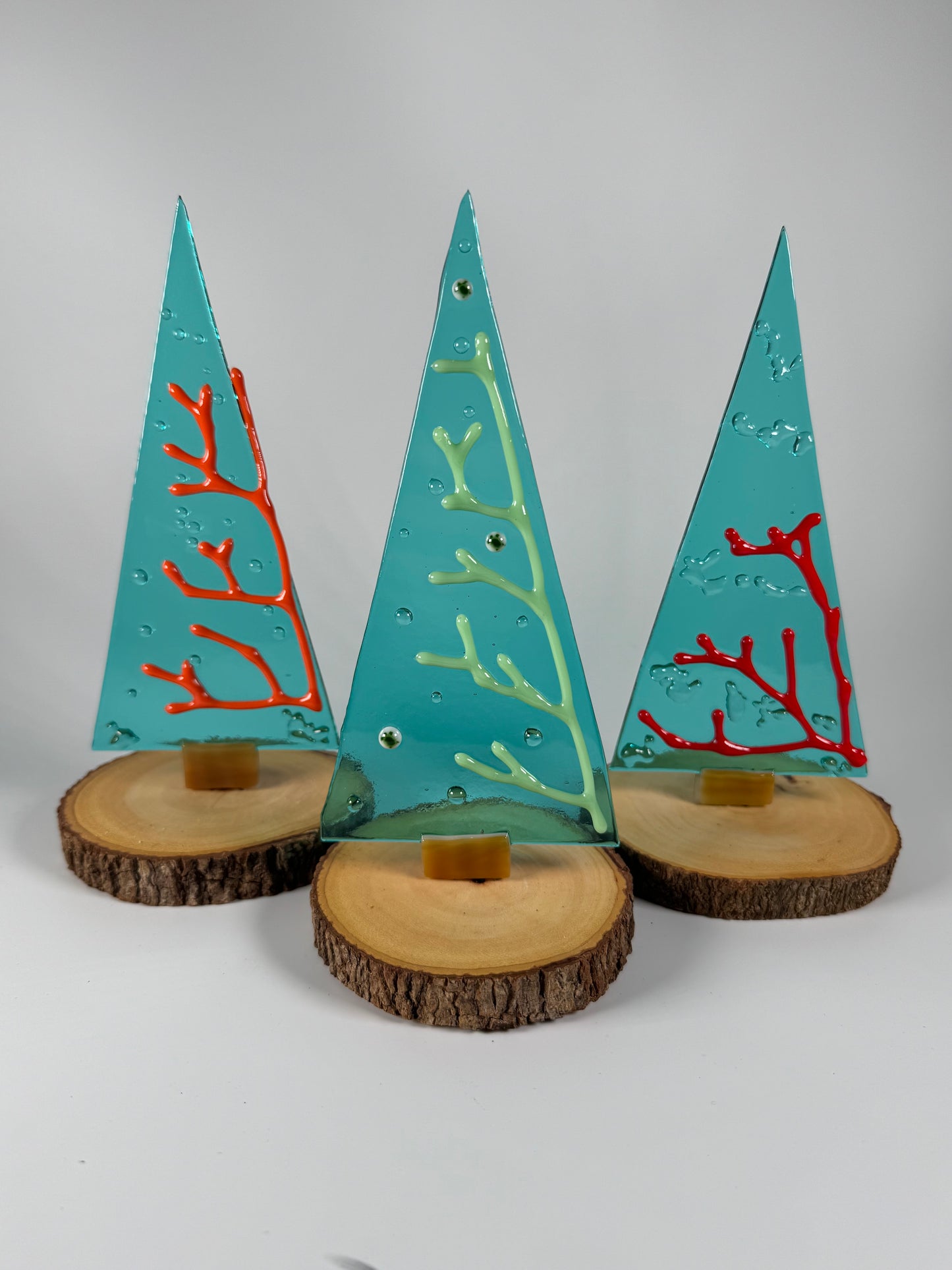 3 glass trees with different colored coral raised from surface made out of glass except wood stand and small wires in base to hold tree upright. Shown on light gray backdrop 