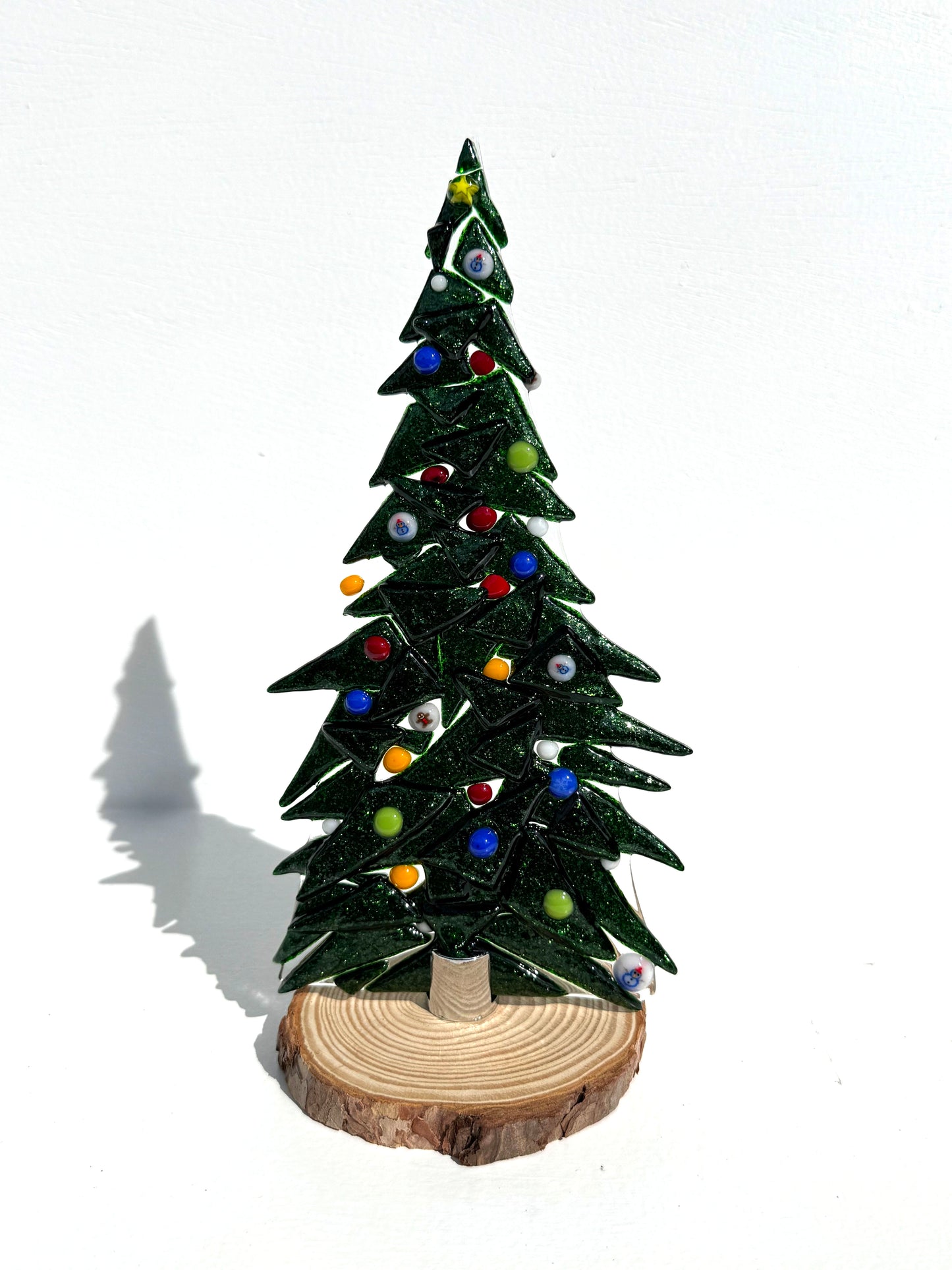Decorative Table top tree made of sparkly dark green glass adorned with colored glass ornaments.  The texture can be felt on one side of the tree.