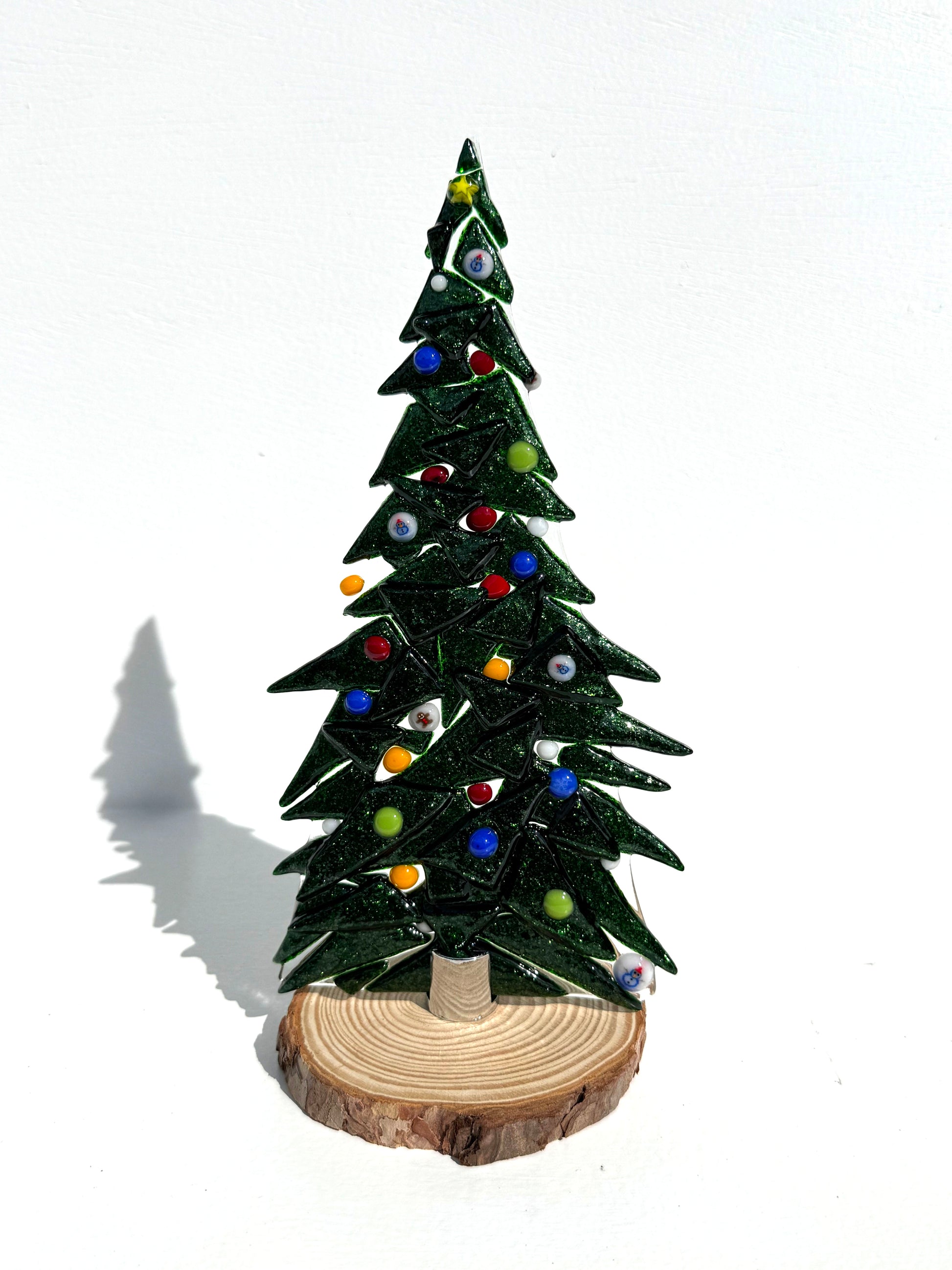 Decorative Table top tree made of sparkly dark green glass adorned with colored glass ornaments.  The texture can be felt on one side of the tree.