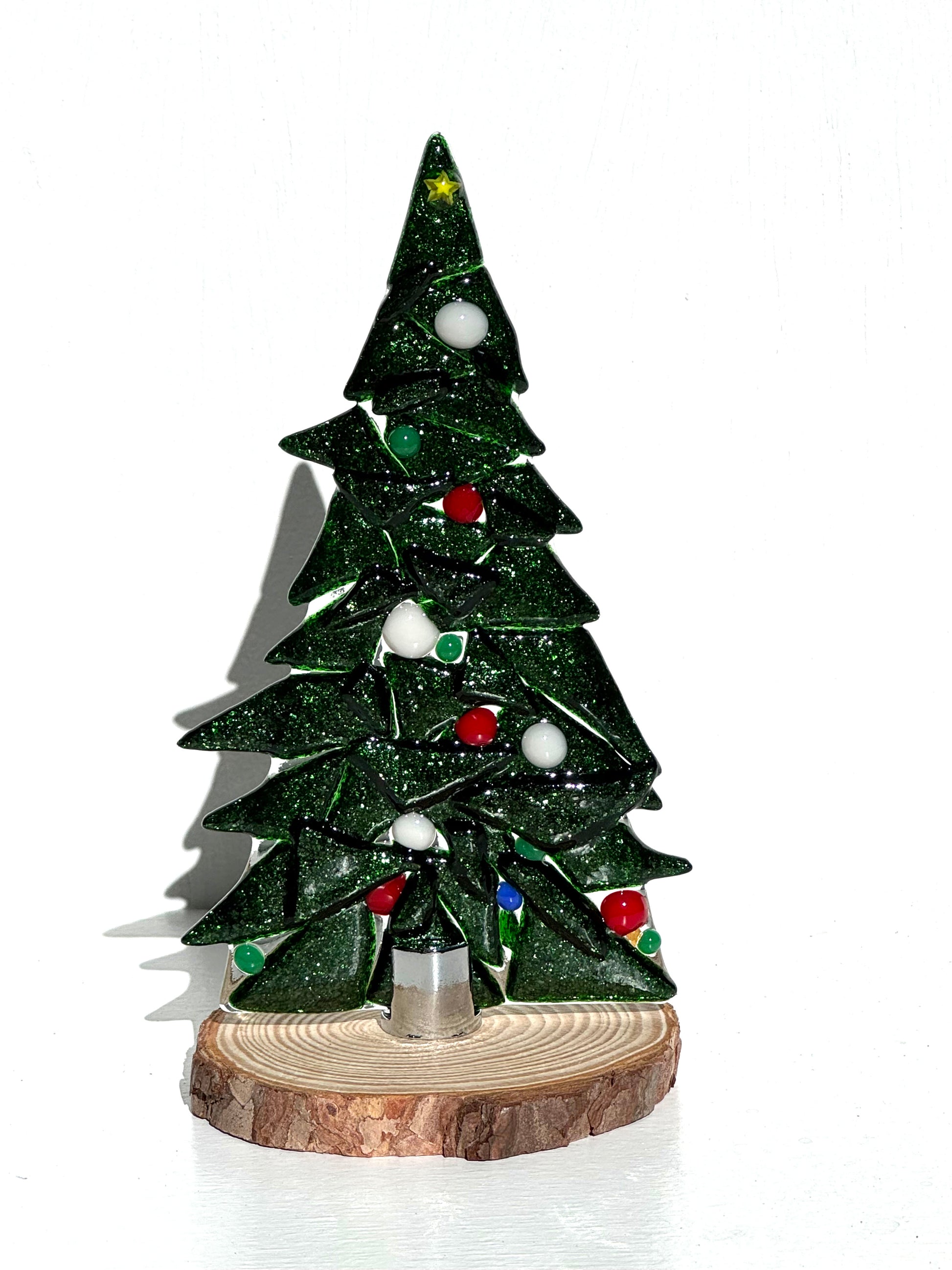 Table top Christmas tree created from dark green shiny glass and decorated with red, white, and green ornaments adorned with a yellow star on the highest bough