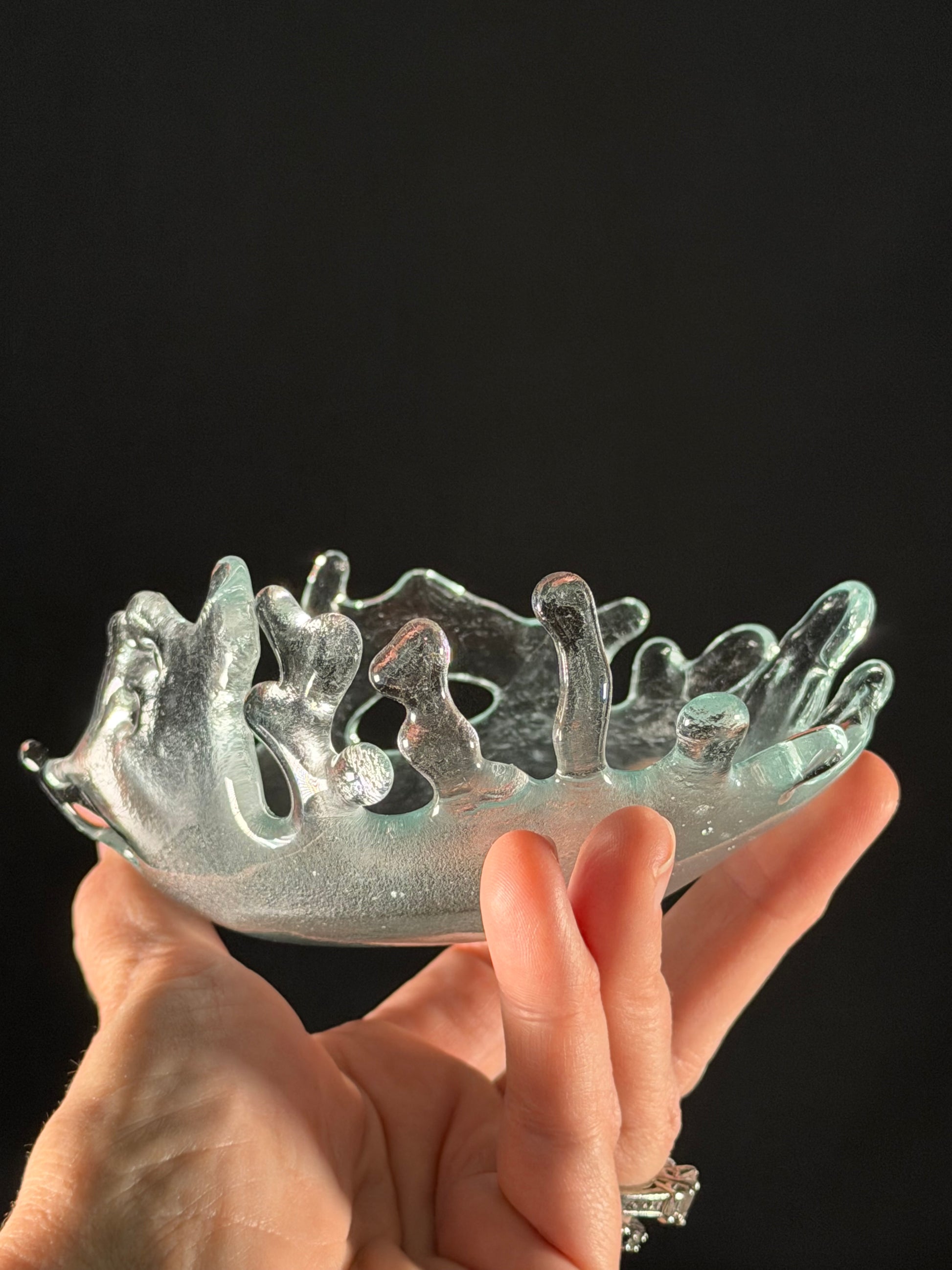 Clear glass object with intricate design held by a hand against a black background