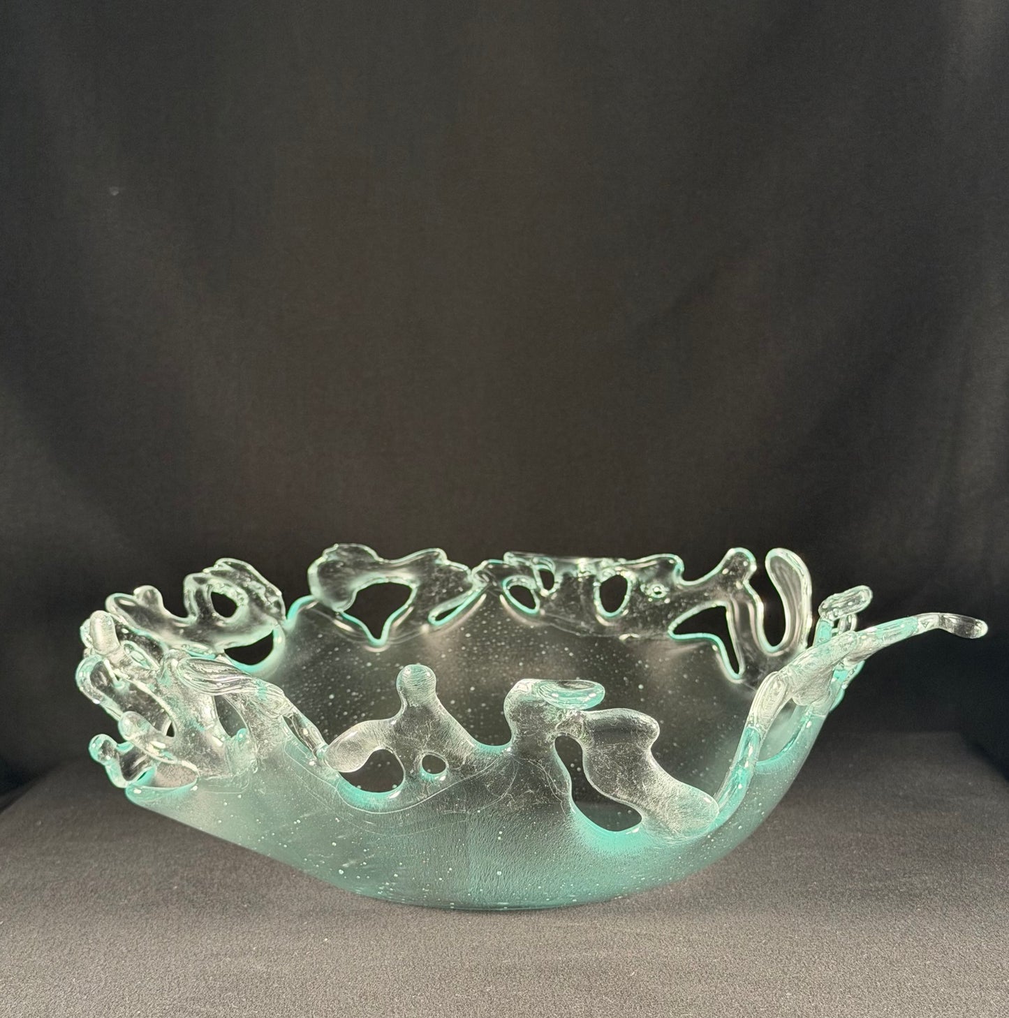 Decorative glass bowl with cut-out designs resembling splashing water on a dark background