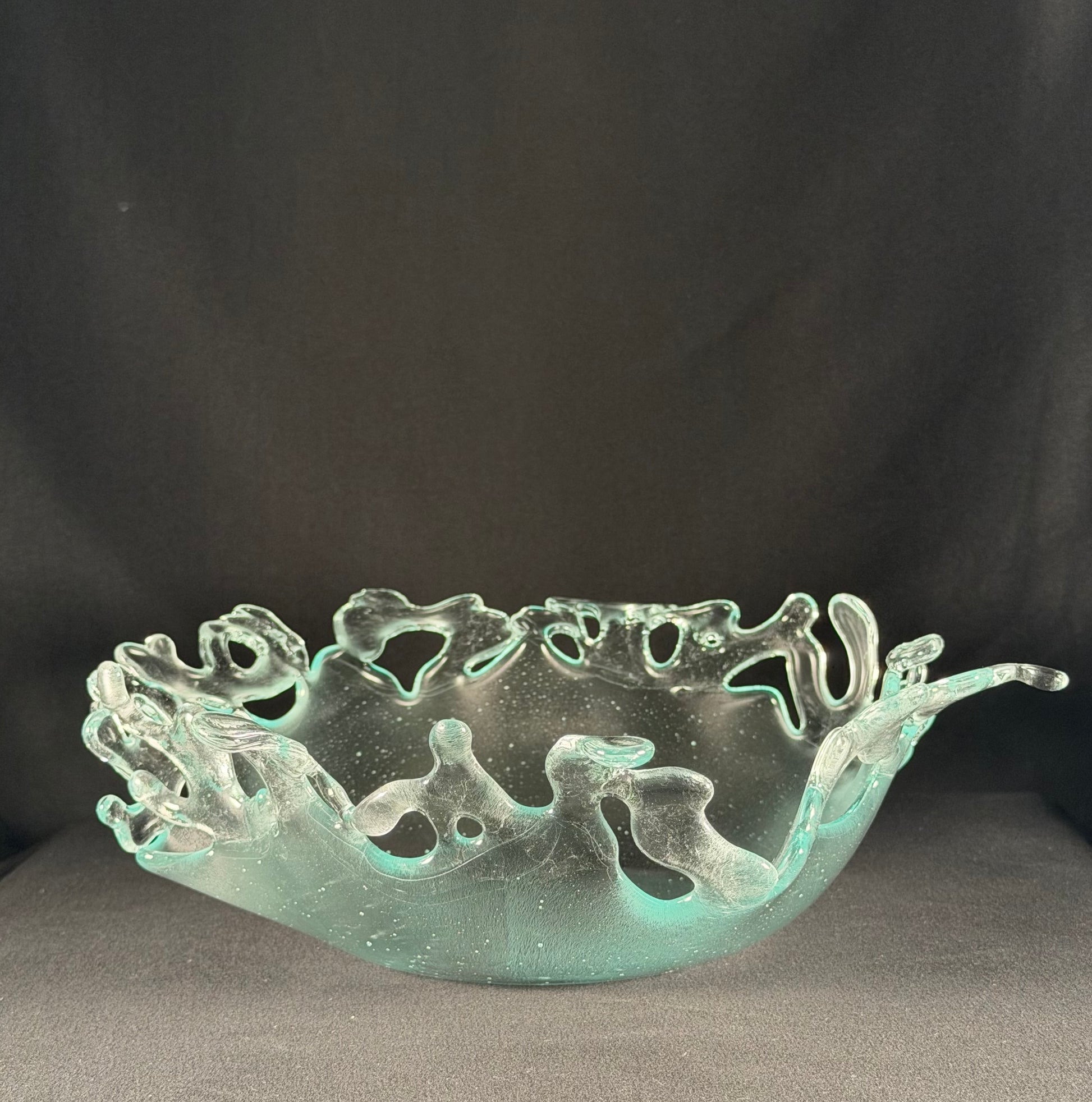Decorative glass bowl with cut-out designs resembling splashing water on a dark background