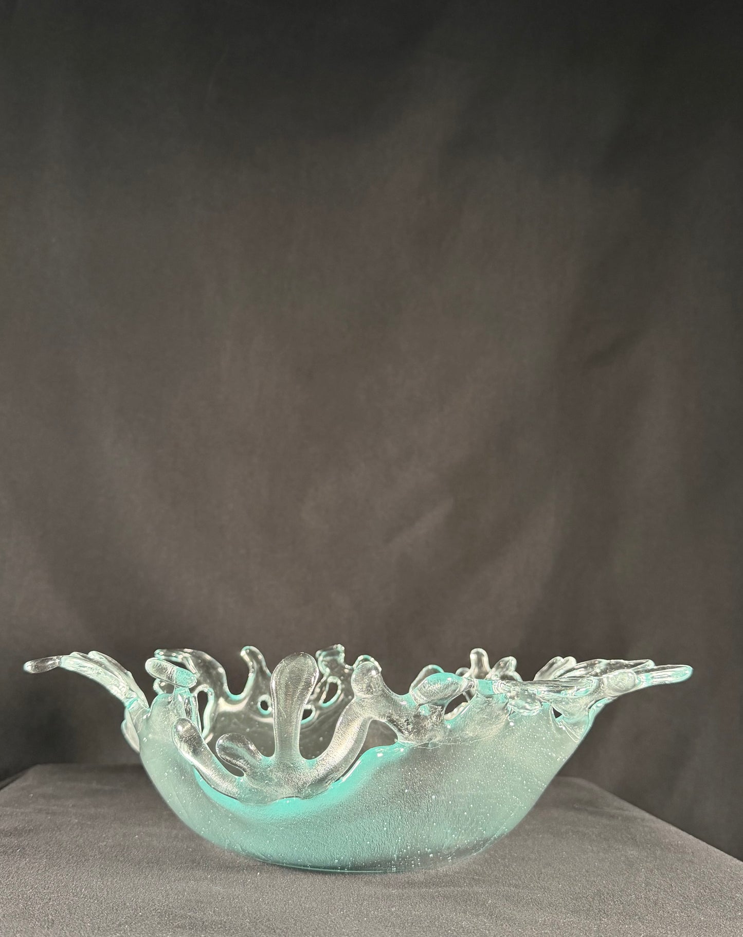 Decorative glass bowl with cut-out designs resembling splashing water on a dark background