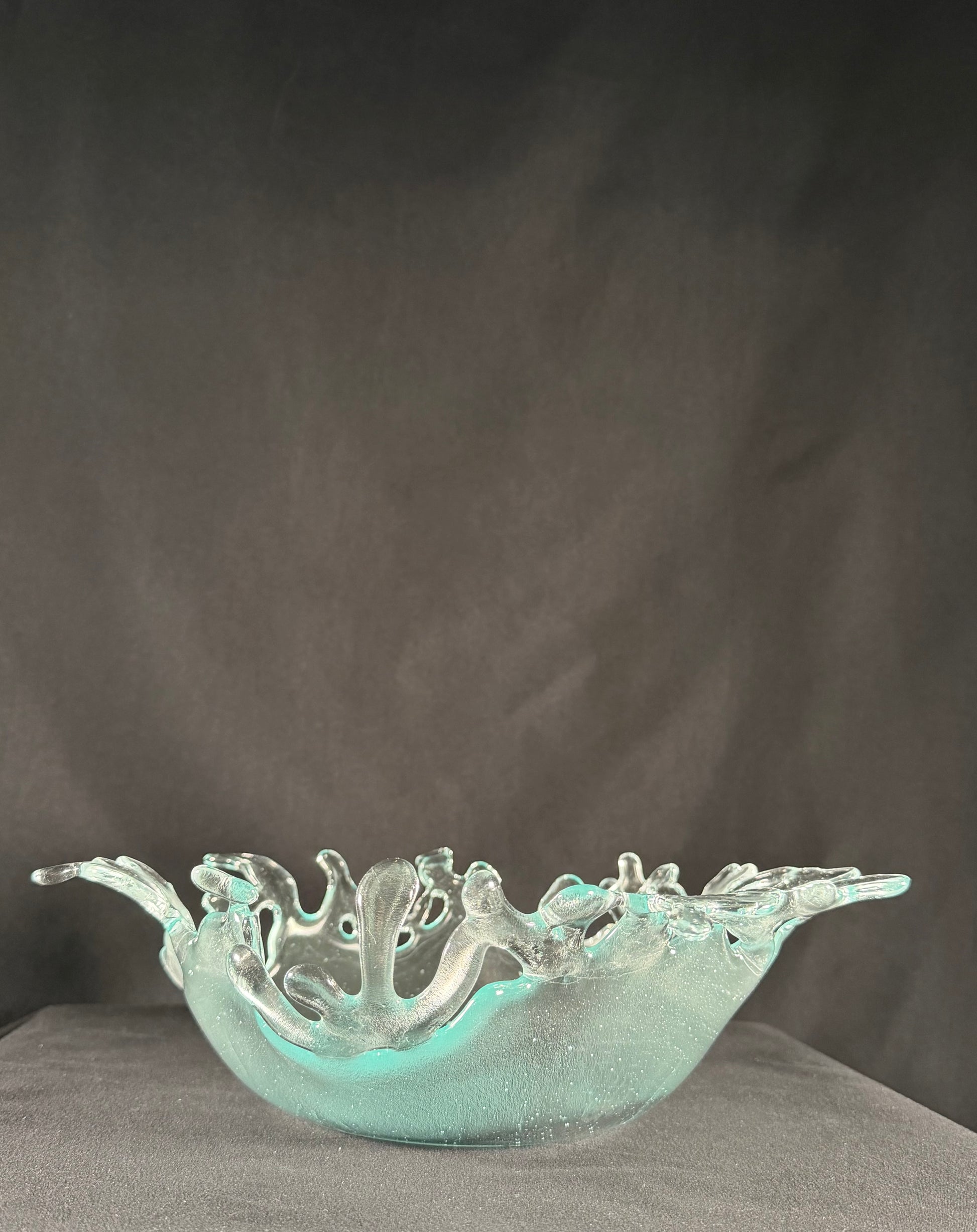 Decorative glass bowl with cut-out designs resembling splashing water on a dark background