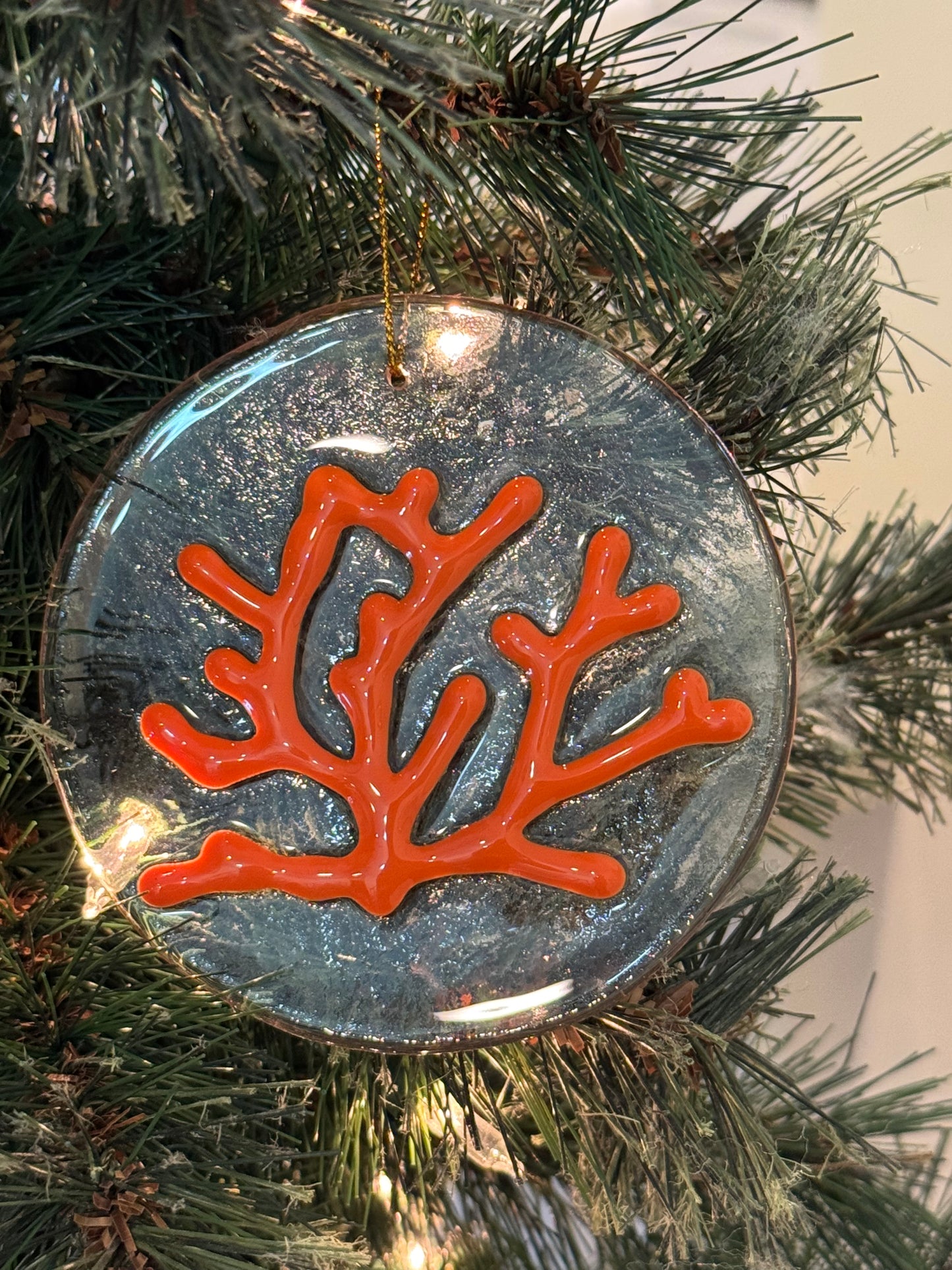Clear glass ornament with raised orange coral design hanging on a Christmas tree 