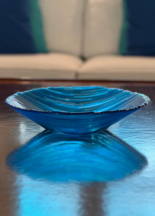 Blue bowl shown on wood coffee table with a white couch in background in front of a window