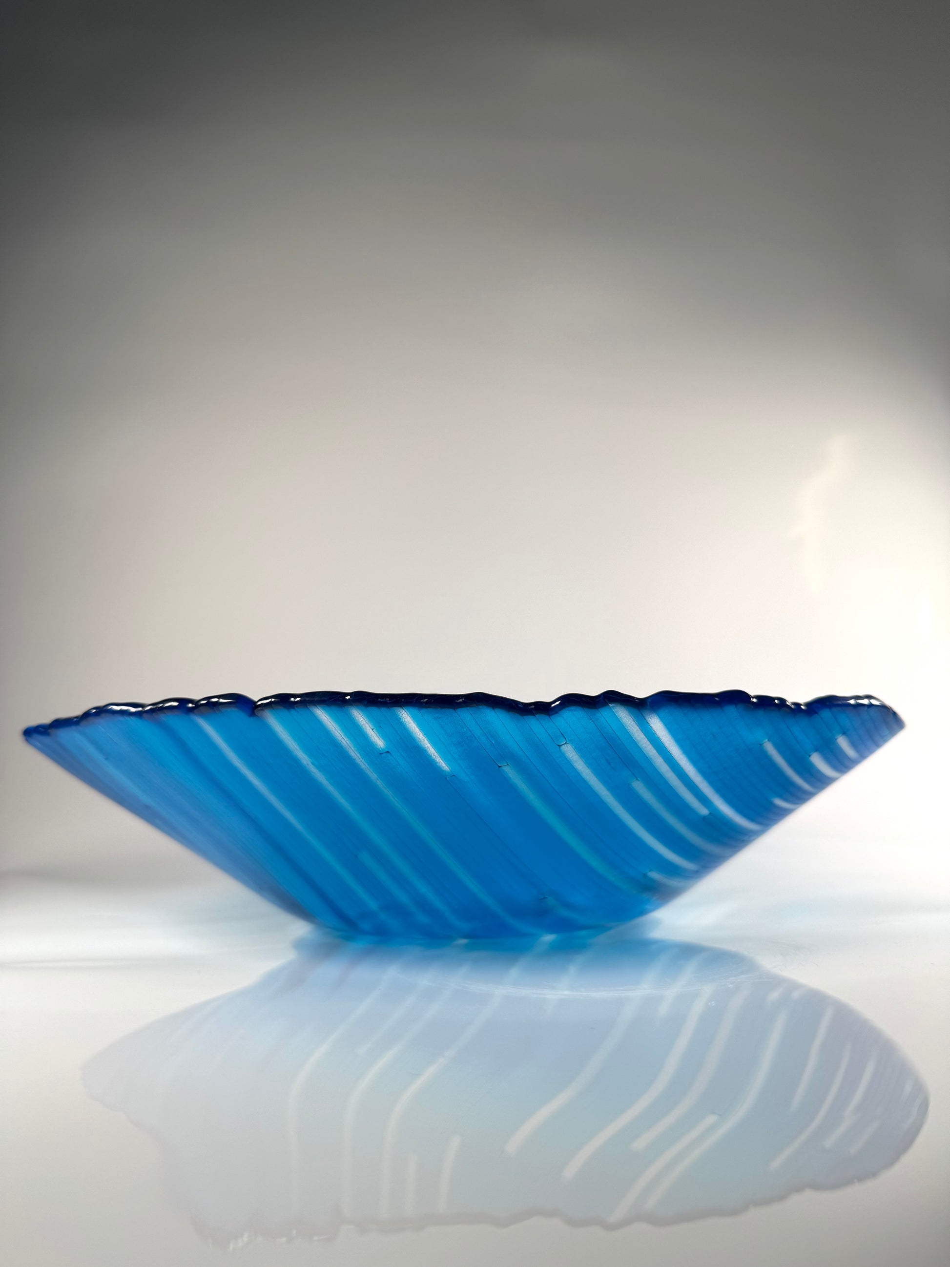 Blue glass bowl on a reflective surface with a gray background
