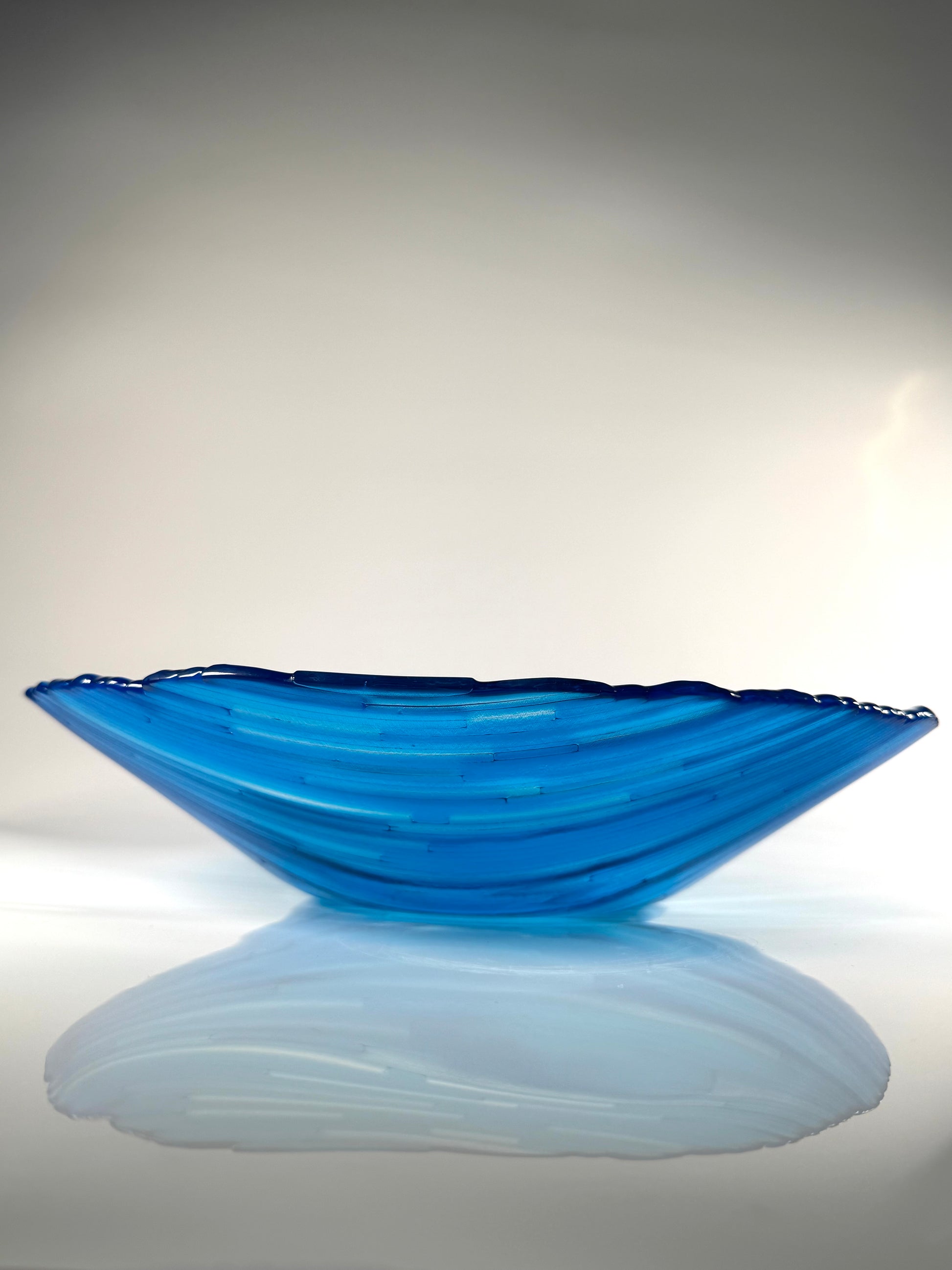 Blue glass bowl on a reflective surface with a light gray background