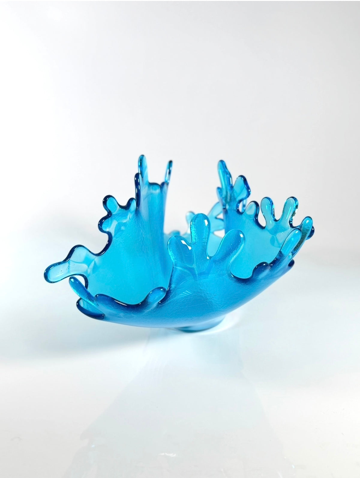 A translucent blue glass bowl with a splashed, water droplet rim, photographed on a clean white studio background.