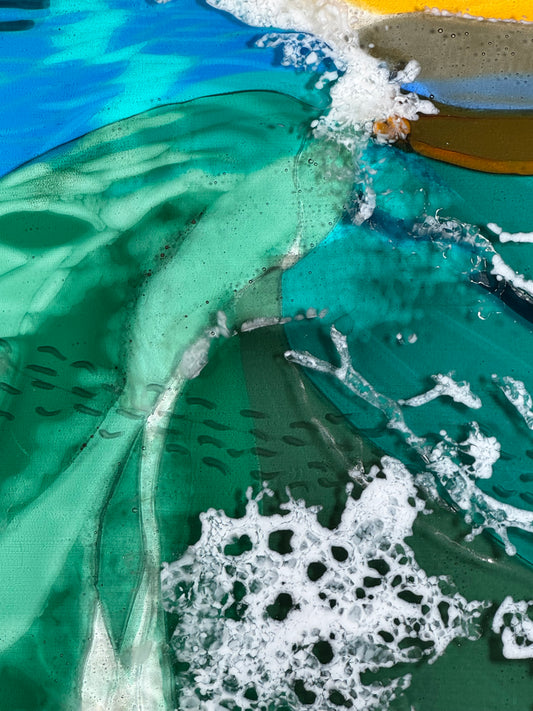 Close-up of a beach scene created from glass with green water, sand, and surf.