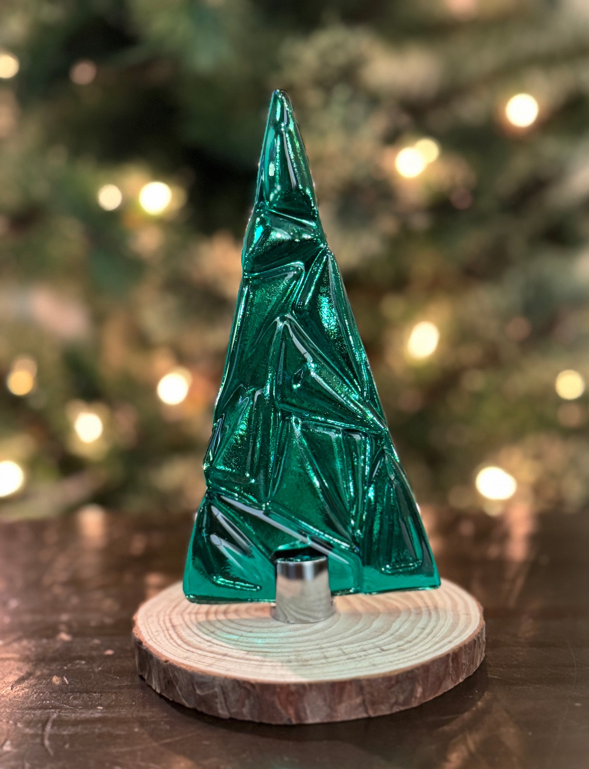 Teal Green glass Christmas tree on a wooden base with blurred Christmas tree in the background