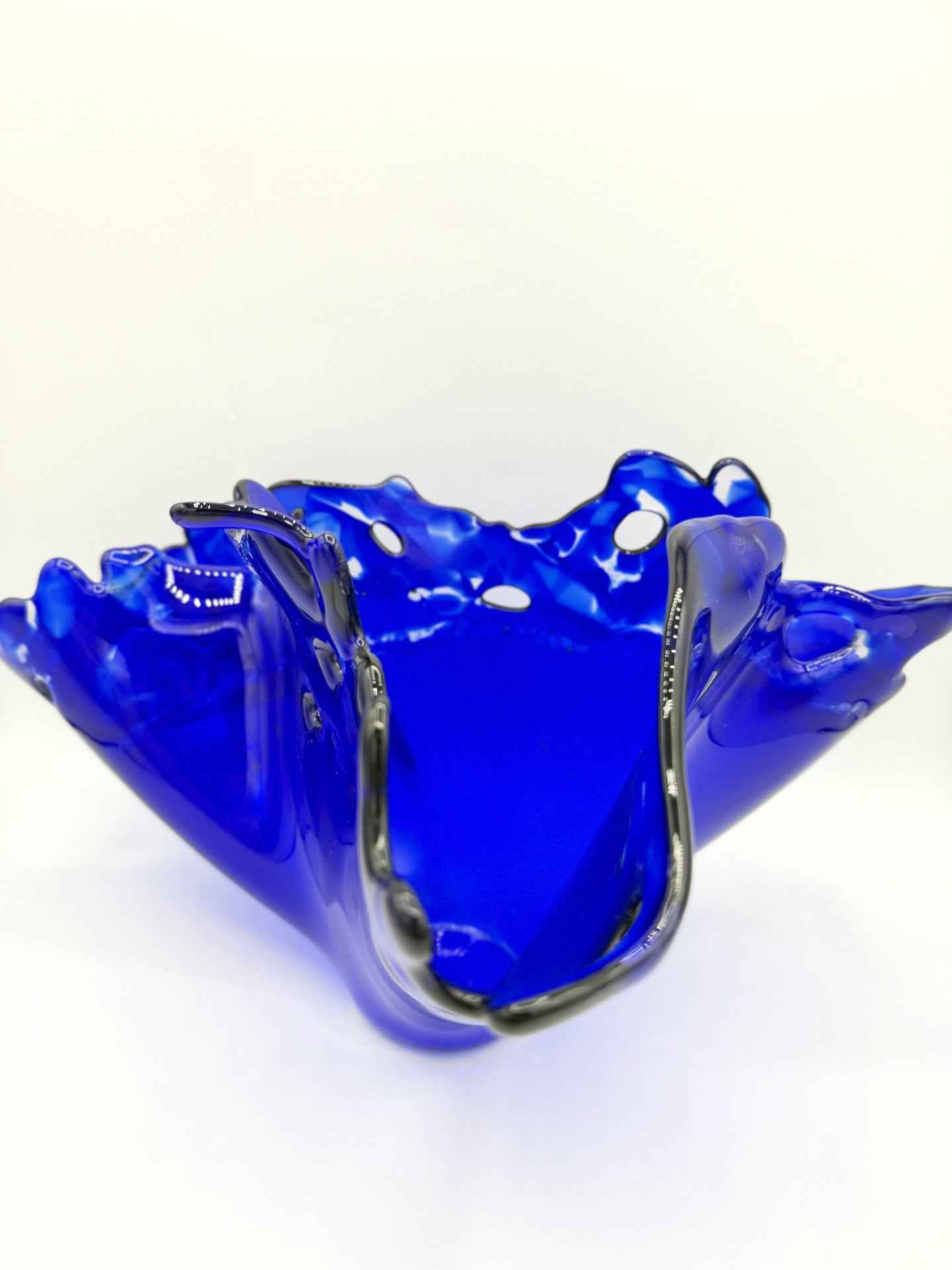  Dark blue glass vase on white background showing a closer look into the vase from the side that is dipped down.